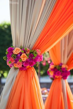 orange and pink flowers are on the back of draping for an outdoor ceremony