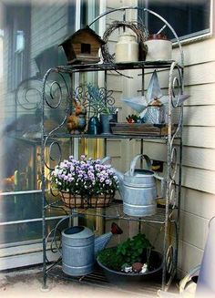 a metal shelf filled with potted plants and watering cans on top of a porch