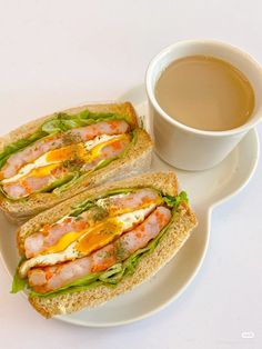 two sandwiches on a plate next to a cup of coffee and saucer with liquid in it