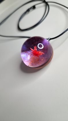 a glass pendant with a red star in the center on a black cord attached to a white surface