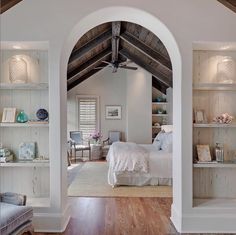 a bedroom with white walls and wooden floors, an arched doorway leading to another room