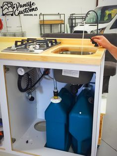 a man standing in front of a kitchen sink with two blue gas tanks under it