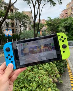 a person holding up a nintendo wii game controller in front of some bushes and trees