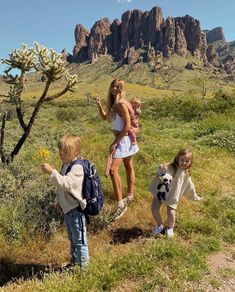 three girls and two boys are standing in the grass near a cactus with mountains in the background