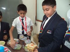 two boys in uniforms are preparing food on a table while another boy is wearing a tie