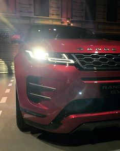 the front end of a red range rover parked in a parking lot with its lights on