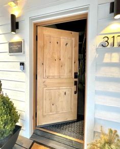 a wooden door is open on the side of a white house with potted plants