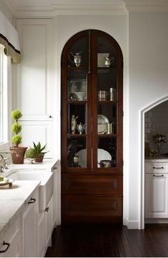 a kitchen with white cabinets and wood flooring next to a large glass doored cabinet