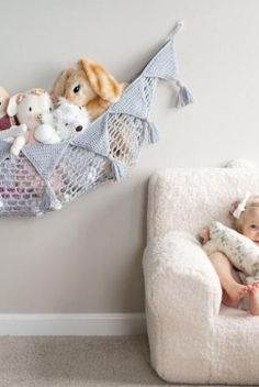 a baby is sitting in a chair with stuffed animals on the wall behind him and holding a pillow