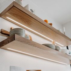 two wooden shelves with plates and bowls on them in a kitchen area that has white walls