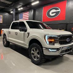 a white truck parked in a garage with an american flag on the wall behind it