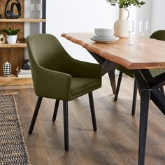 a wooden table with two green chairs next to it and a white vase on top