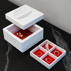 two white boxes with red trays filled with jewelry on top of a black table