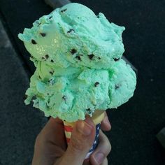 a hand holding an ice cream cone filled with mint green chocolate chip icecream