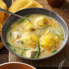 a bowl of soup with dumplings and green beans on the side next to a spoon