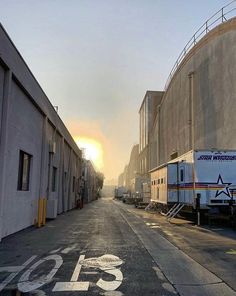 the sun is setting on an empty street in front of some storage buildings and trucks