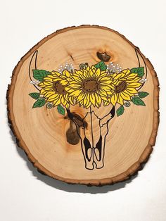 a cow skull with sunflowers painted on it's face sits on a wood slice