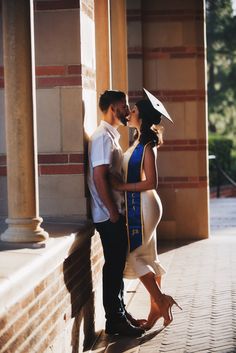 a man and woman standing next to each other on a brick wall with columns in the background