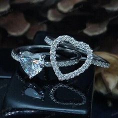 two heart shaped diamond rings on top of a black box with shells in the background