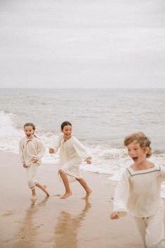 three children running on the beach near the ocean