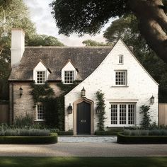 a white brick house surrounded by trees and hedges in front of a gated driveway