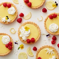 lemon tarts with whipped cream, raspberries and flowers on a white surface