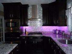 a kitchen with black cabinets and purple lights on the backsplash is pictured in this image