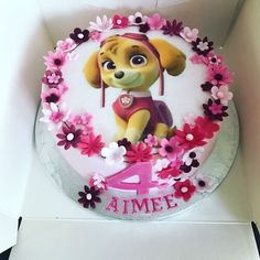 a birthday cake with a dog on it and pink flowers around the edges, in a box