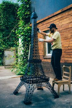 a man standing next to the eiffel tower in front of a wooden building