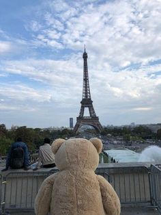 a teddy bear sitting in front of the eiffel tower with people looking on