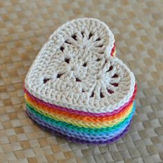 a crocheted heart is sitting on a woven mat with the colors of the rainbow