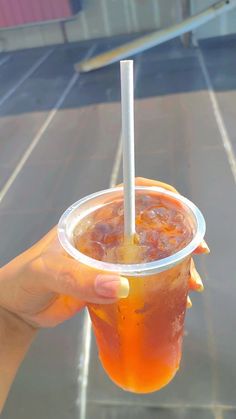 a person holding up a plastic cup with a straw in it and orange liquid inside