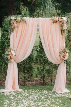 an outdoor wedding ceremony setup with pink drapes and flowers on the grass, surrounded by greenery