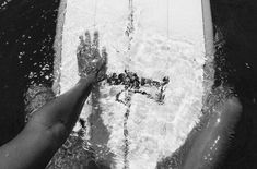 two people on a surfboard in the water with their hands out to touch them