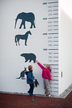 two children are standing next to a tall growth chart with animals on it and one child is measuring the height