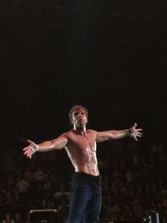 a shirtless man standing on top of a skateboard in front of a crowd