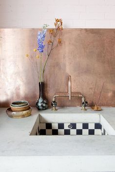 a white sink sitting under a faucet next to a vase with flowers in it