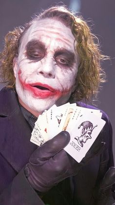 a man dressed as the joker holding playing cards in his hands and wearing black gloves