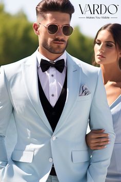 a man in a white suit and bow tie standing next to a woman wearing sunglasses