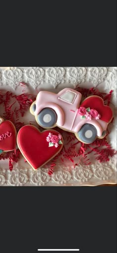 two decorated cookies in the shape of cars and hearts on a lace doily with pink flowers