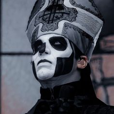 a man with black and white face paint is wearing a cross on his head while standing in front of a brick wall