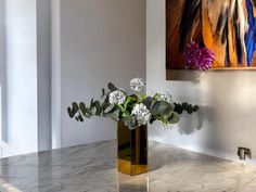 a gold vase with flowers in it on a marble countertop next to a painting