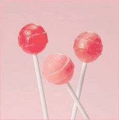 two red lollipops sitting on top of each other in front of a pink background