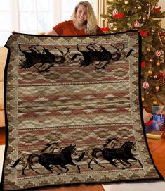 a woman is holding up a quilt with horses on it in front of a christmas tree