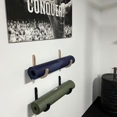 there are two yoga mats hanging on the wall next to some dumbs and a sign that says conquer