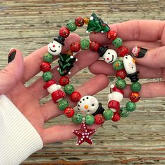 a person holding some christmas themed beads in their hand on a wooden table with snowmen