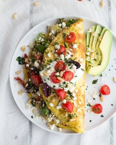 an omelet with tomatoes, avocado and other toppings on a white plate