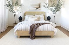 a bed with white sheets and pillows in a bedroom next to two vases on either side of the bed