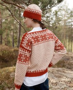 a woman standing in front of a tree wearing a red and white sweater