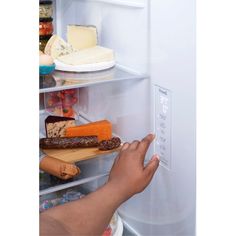 a person reaching into an open refrigerator with cheese and meat on the shelf in front